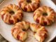 Anneaux de pommes entourés de pâte feuilletée dorée et saupoudrés de cannelle sur une assiette.