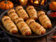 Saucisses momies en pâte feuilletée dorée, avec des yeux en moutarde et olive, présentées dans un décor d’Halloween.